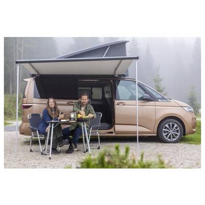 Couple sits at a folding table under a pop-up awning beside a tan camper van in a misty outdoor campsite.<br>