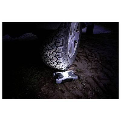 A car tire is pressing on a small rugged remote-controlled vehicle on muddy ground at night, crushing it under the wheel.