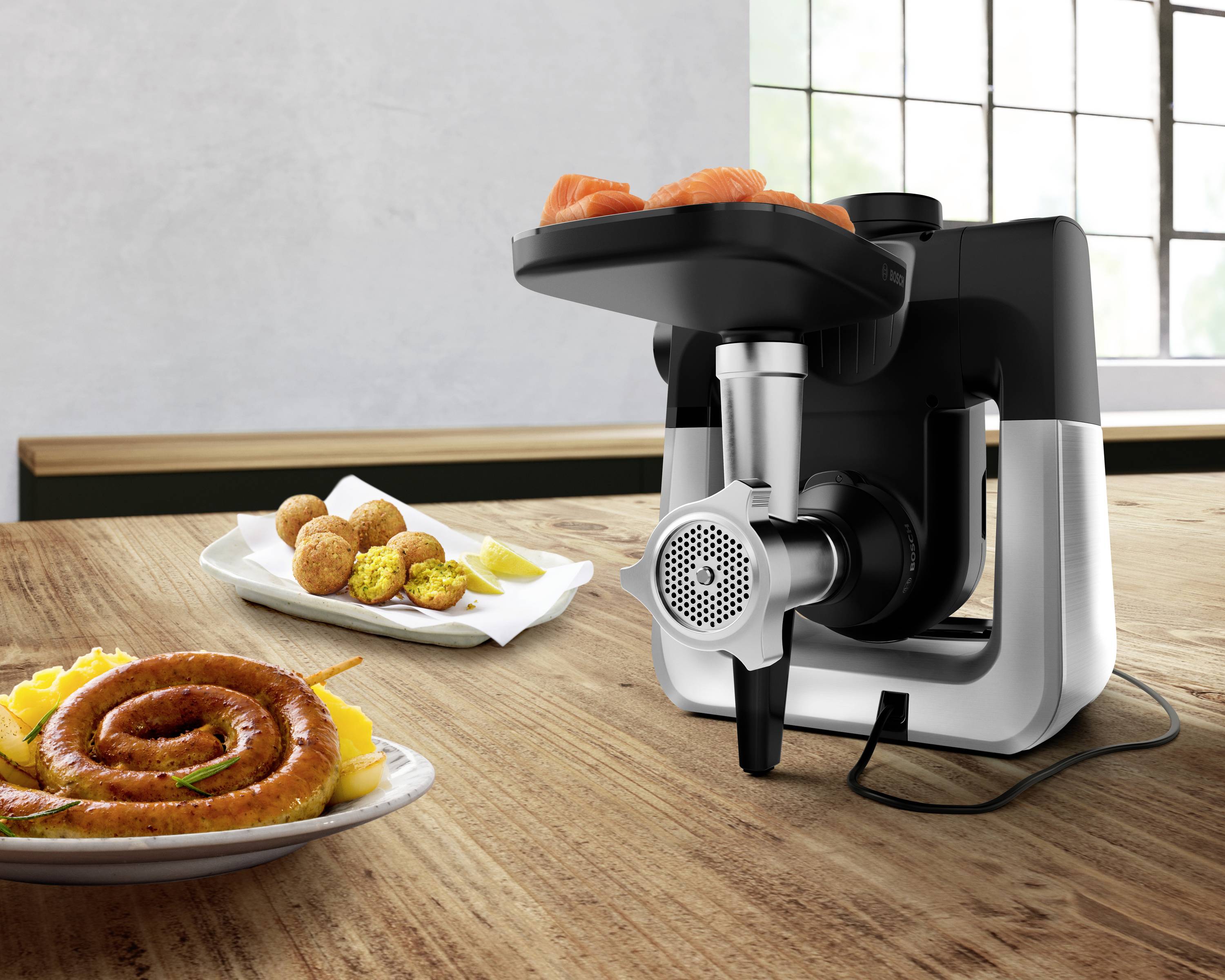 A sleek kitchen meat grinder on a wooden counter, with fresh ingredients like sausages, meat, and vegetables ready for processing.