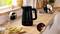 'Black electric kettle on a kitchen counter with labeled features: ergonomic handle, push-button lid, and power indicator light.'