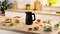 A black electric kettle on a kitchen counter surrounded by various dishes and hot beverages. Sunlight filters through a window, creating a warm ambiance.