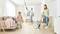 A family is using vacuum cleaners to clean a bright living room. A woman vacuums the floor, a man cleans the ceiling, and a child helps.
