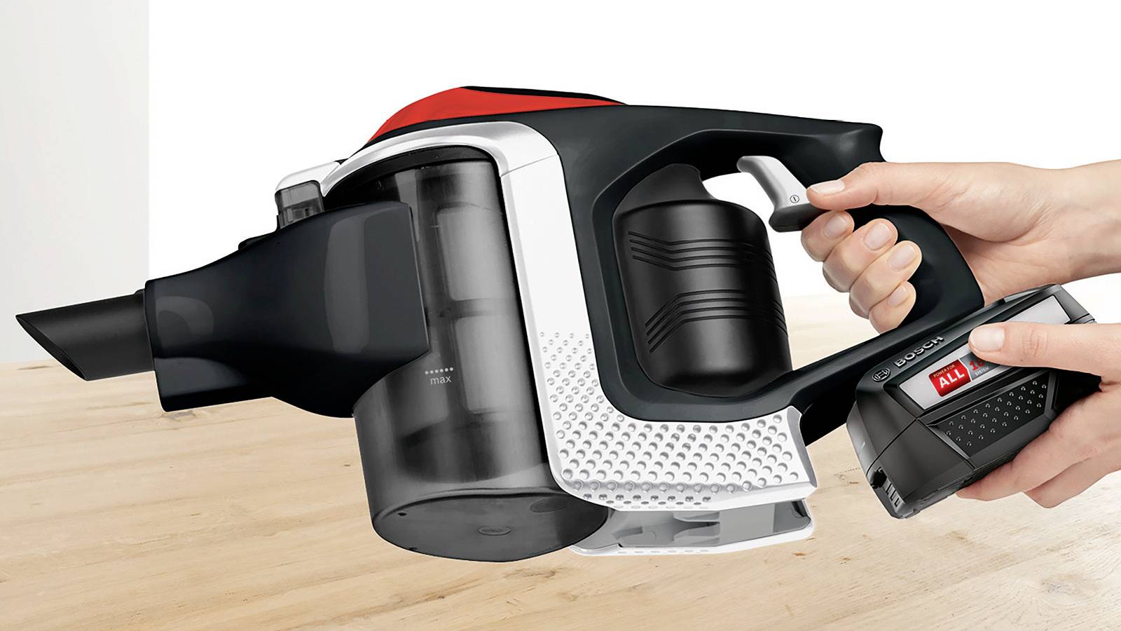 A person holds a cordless handheld vacuum cleaner over a wooden surface, showing the battery being inserted into the device.