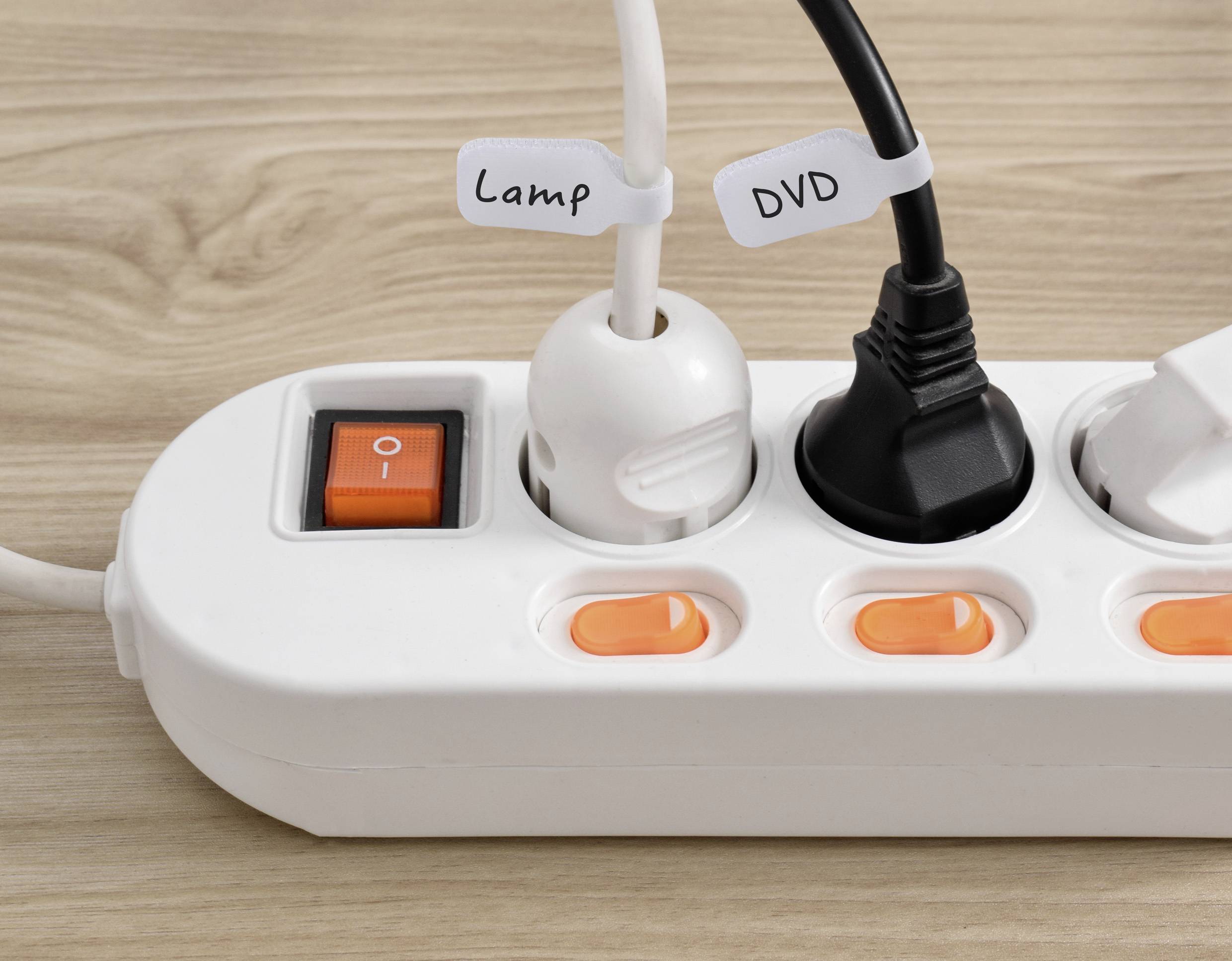 A white power strip with a red switch and three plugs: one labeled 'Lamp,' another labeled 'DVD,' all on a wooden surface.