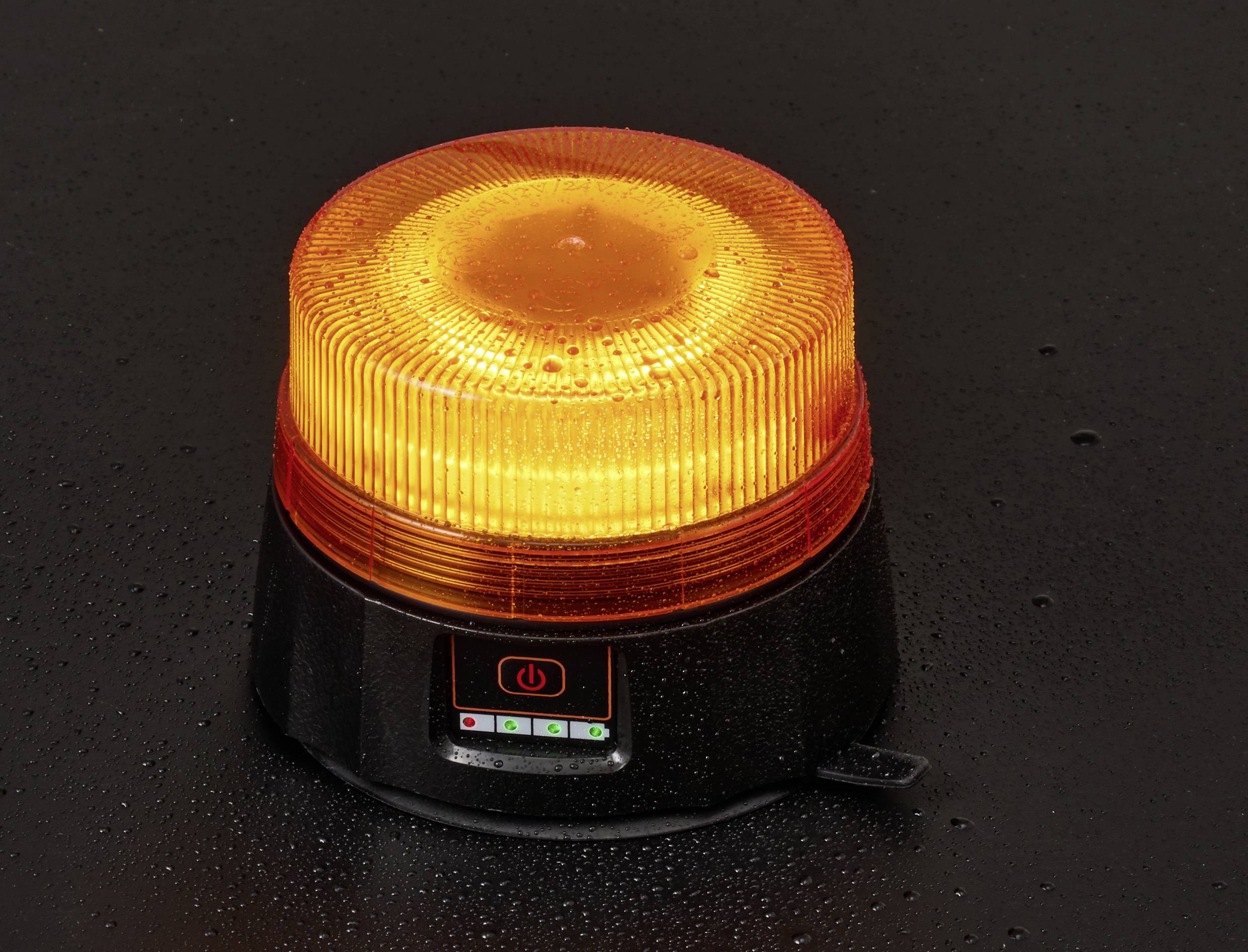 An orange warning beacon with a power button, on a dark, wet surface, indicating it's turned on, likely for safety or alert purposes.