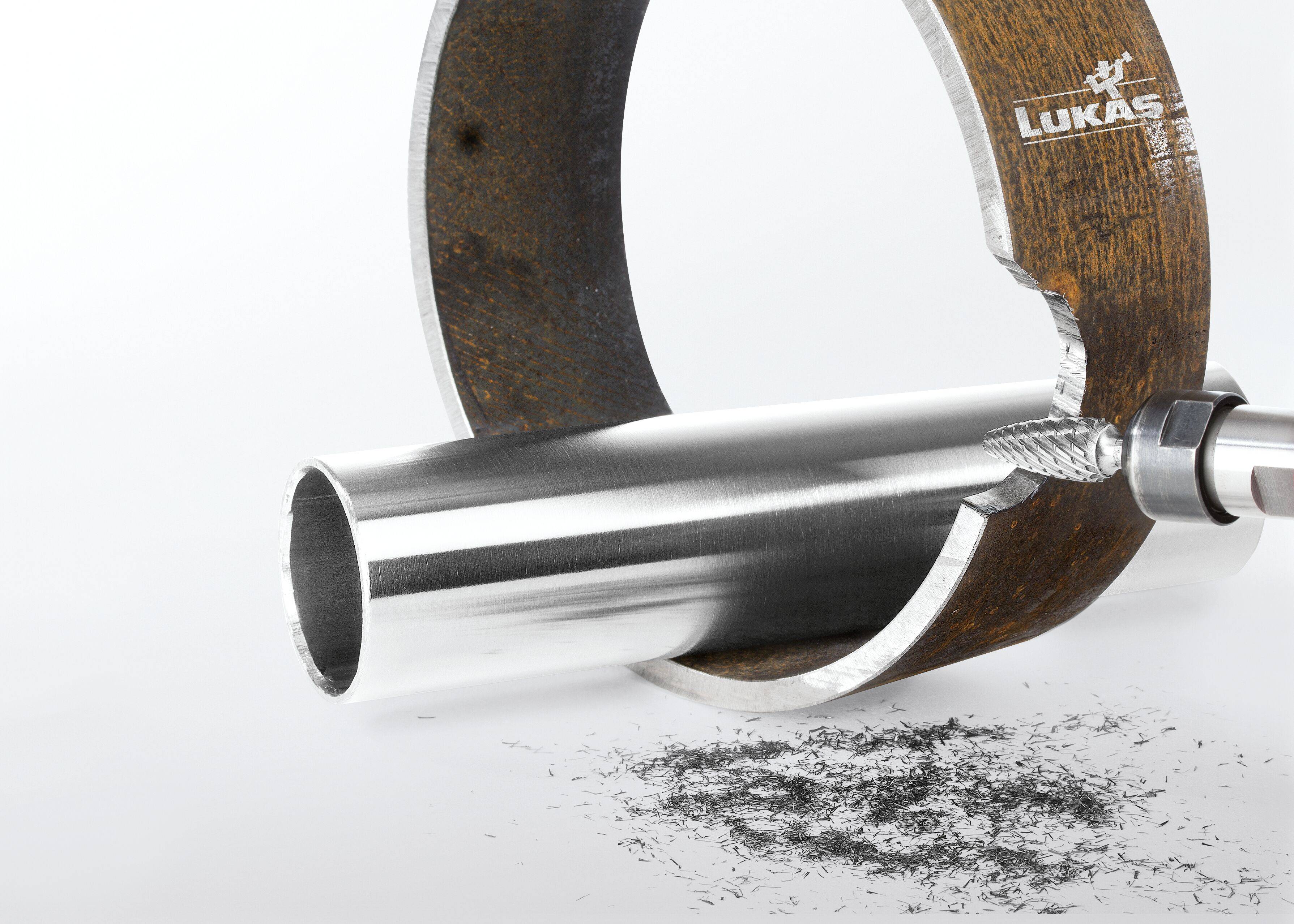 A pipe being deburred with a rotary tool, leaving a smooth finish. Metal shavings rest below, indicating recent work.