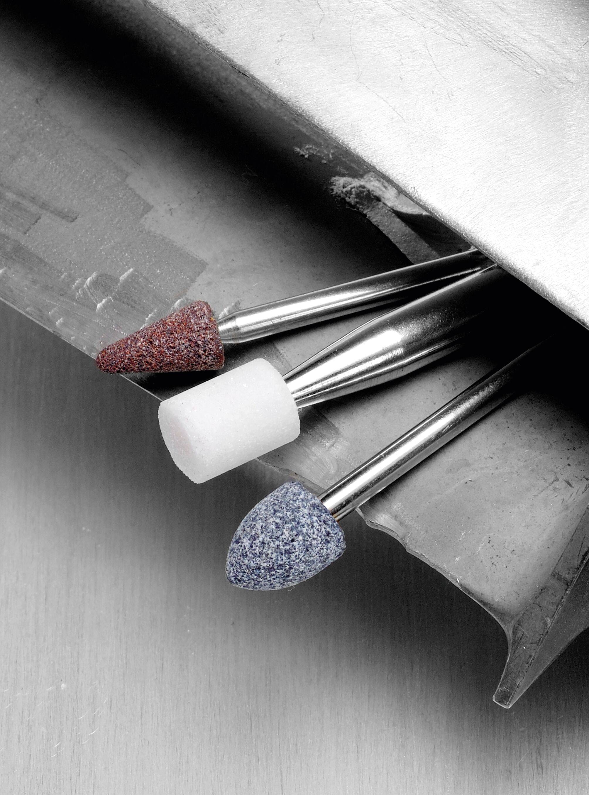 Three grinding heads with different textures and colors rest on a metallic surface, showcasing tools for smoothing or polishing materials.