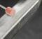 A pink abrasive tool polishes a metallic surface, smoothing the edges of a rectangular metal bar against a dark background.