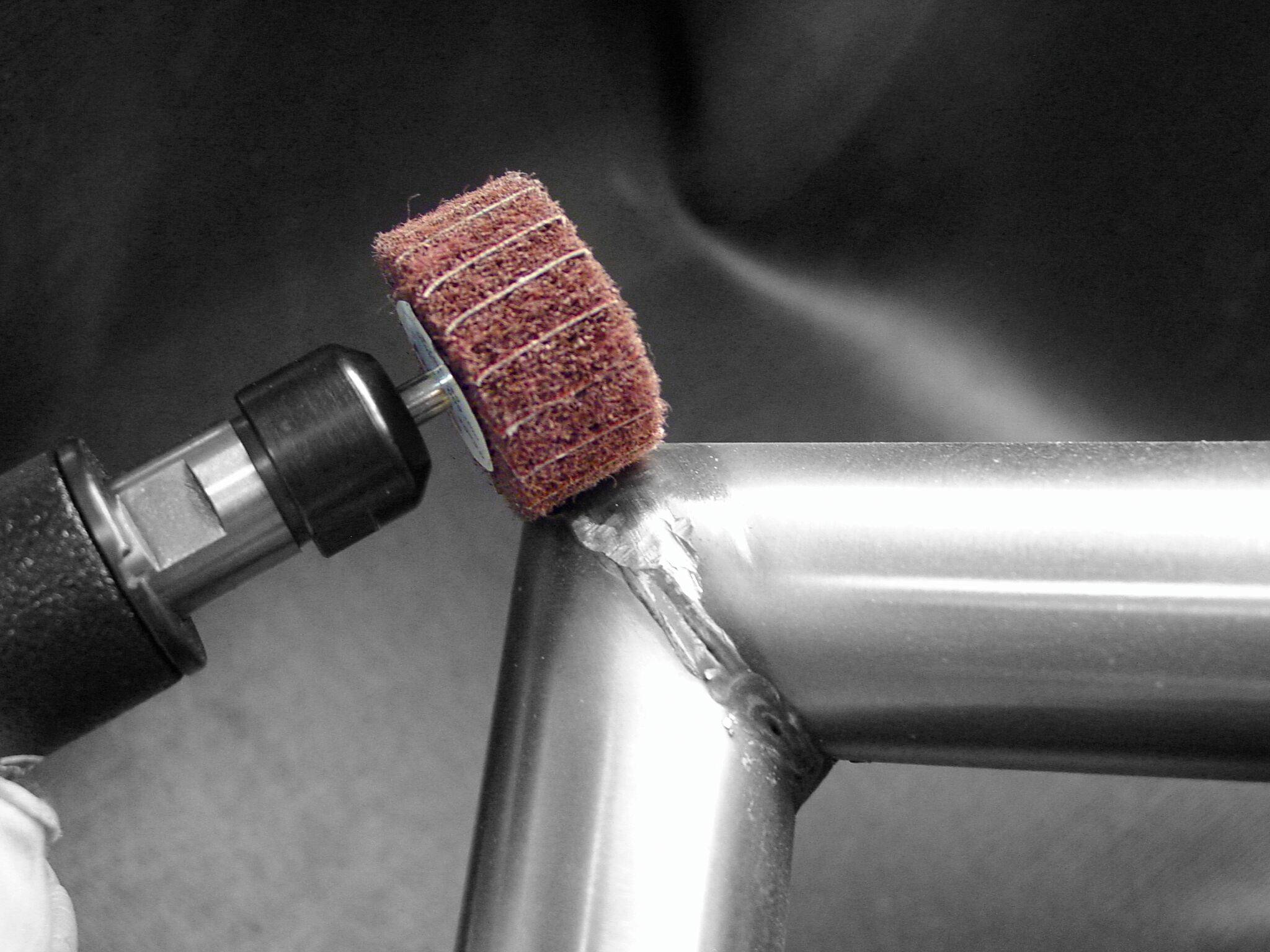 'Abrasive tool polishing a metal welded joint on a stainless steel frame, smoothing surface for finishing.'