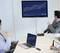 Three professionals in a meeting room examine a presentation with line graphs and statistics displayed on a screen.
