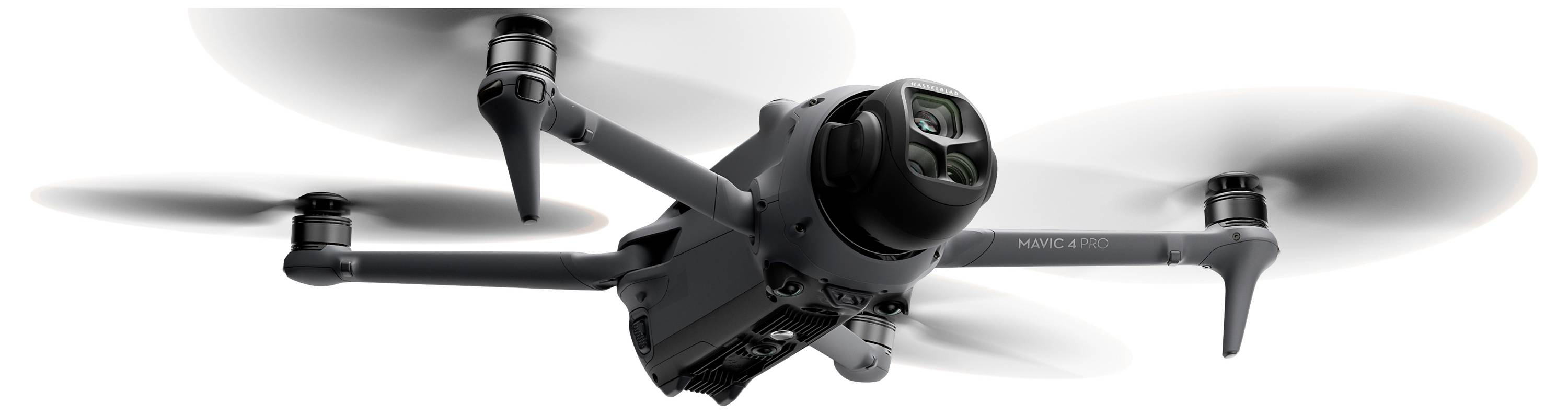 A quadcopter drone flying, showing four spinning propellers and camera in the center. The drone appears sleek and modern.