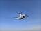 A white quadcopter drone flying against a clear blue sky, showcasing its propellers and camera, indicating modern aerial technology.