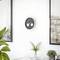 A minimalistic room features a wall clock with two smaller dials in its face, framed abstract art, and a tabletop with ferns and candles.