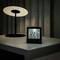 A digital clock on a bedside table displays '12:21', with temperature '29°C'. A lamp with a round shade is lit in the background.