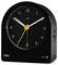 A black Braun analog alarm clock with a white hour hand, yellow minute hand, and orange second hand shows 7:08. It has an alarm button.