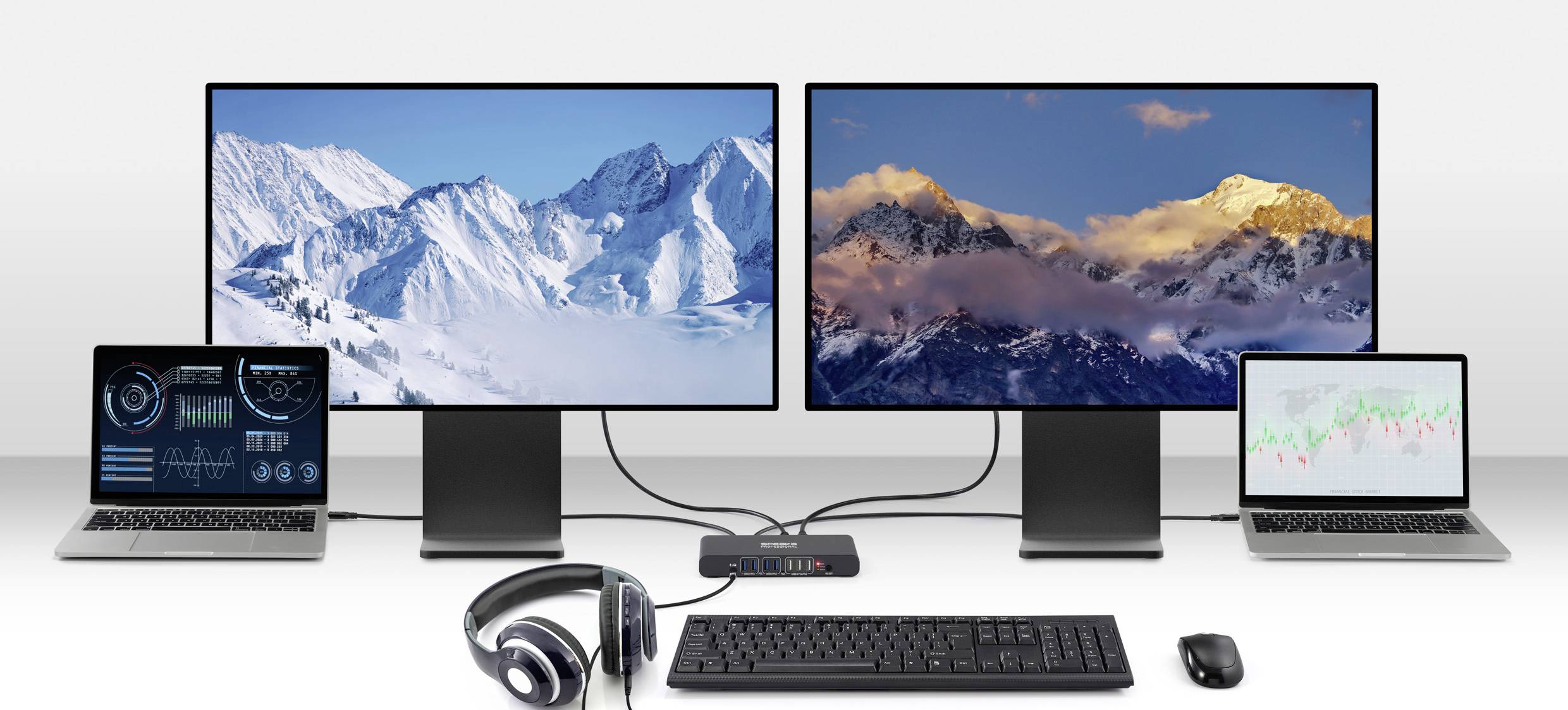 A dual-monitor setup connected to two laptops, displaying snowy mountains and charts. A keyboard, mouse, and headphones are placed in front.