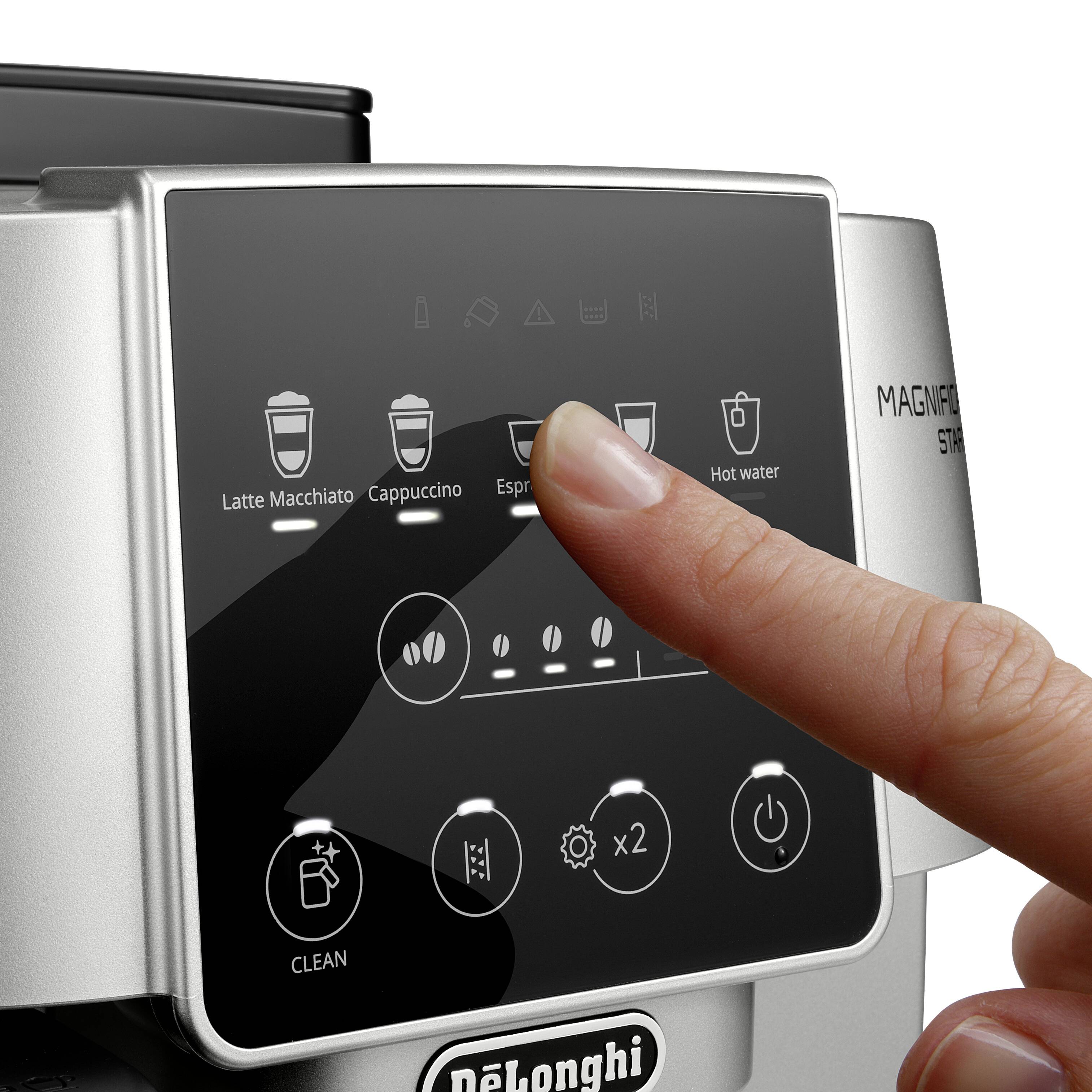 A finger selects the 'Espresso' option on a DeLonghi Magnifica Start coffee machine display. Other options include latte macchiato and cappuccino.