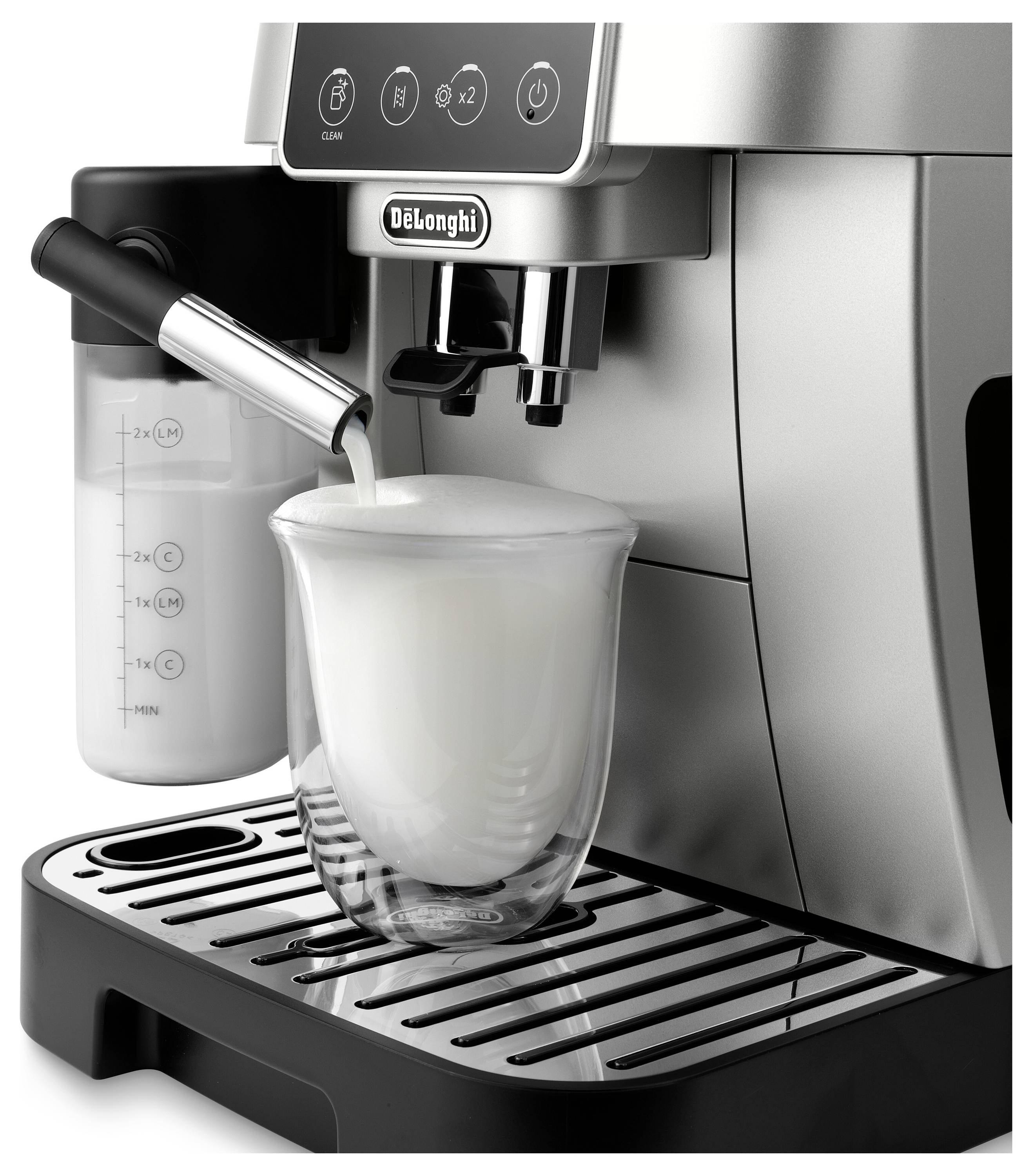 A silver espresso machine dispensing milk foam into a clear glass cup on its tray, with a milk container attached to the side.