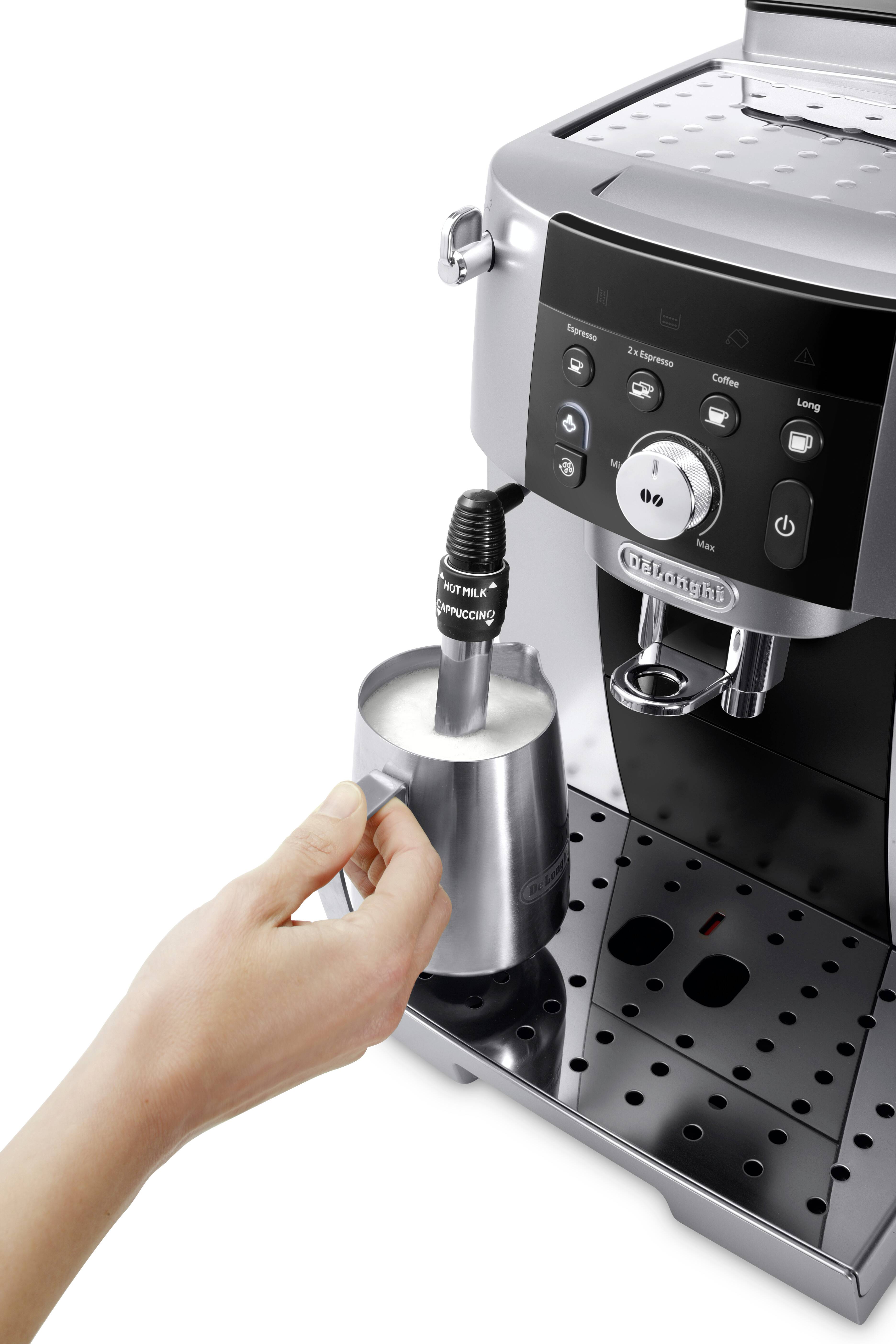 A person froths milk with a stainless steel frothing mug using a modern espresso machine's steam wand, preparing a beverage.