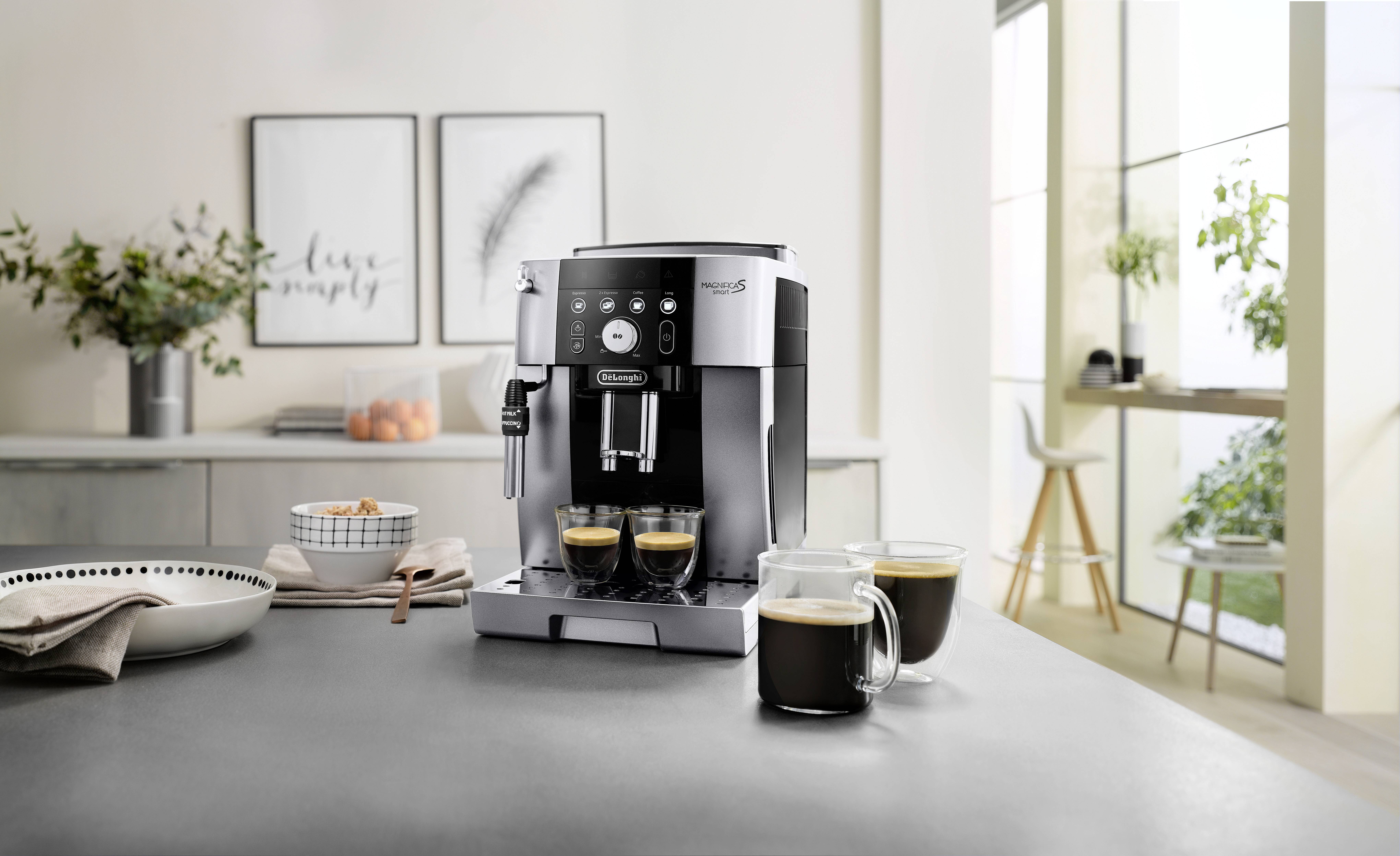 A modern coffee machine on a kitchen counter surrounded by glass mugs filled with coffee, under soft natural light through large windows.