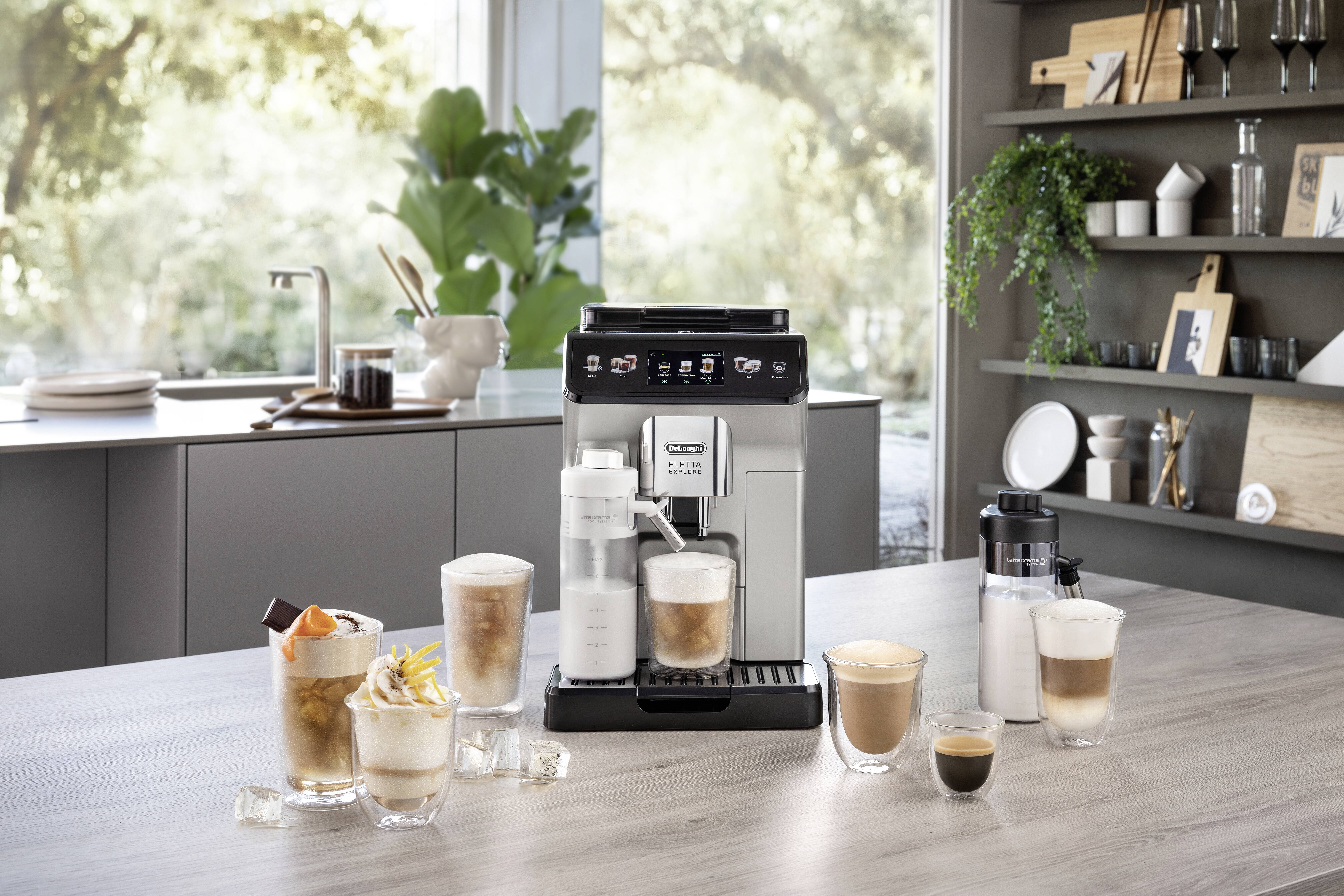A coffee machine on a kitchen counter surrounded by various coffee drinks in glasses, with a sunny view of trees through the window.
