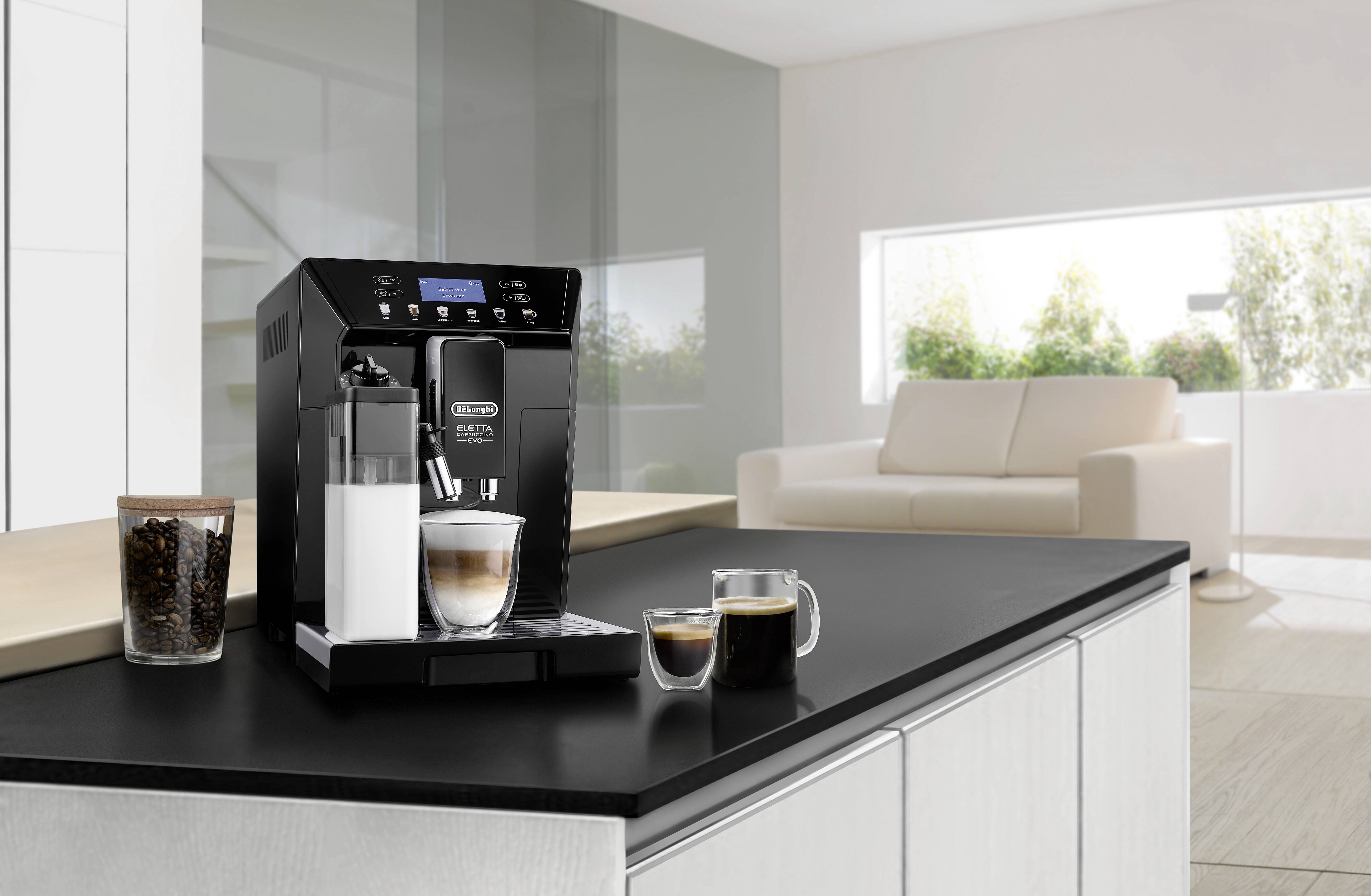 A modern coffee machine on a kitchen counter brews espresso into a glass cup. Two additional cups of coffee are beside it.