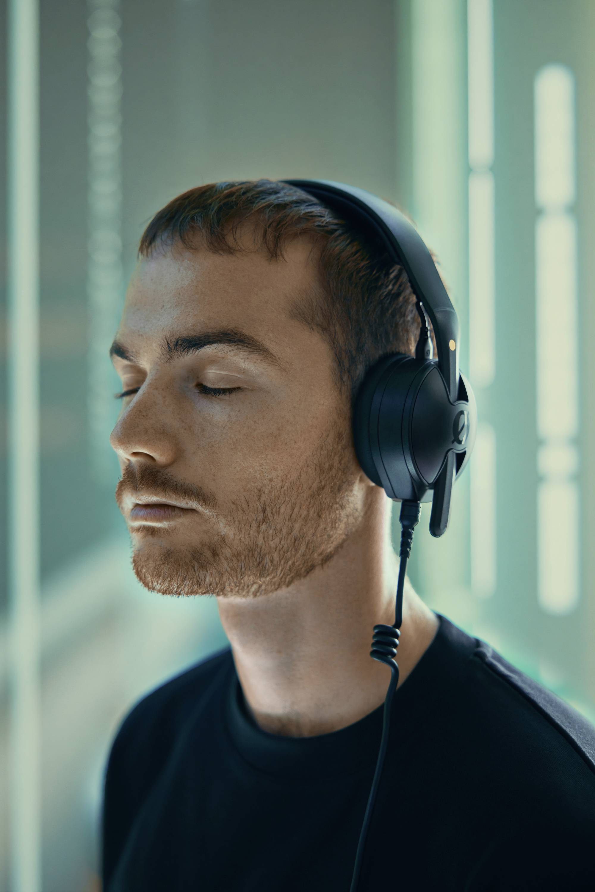 A person with closed eyes wearing large headphones, appearing relaxed, in a softly lit environment.