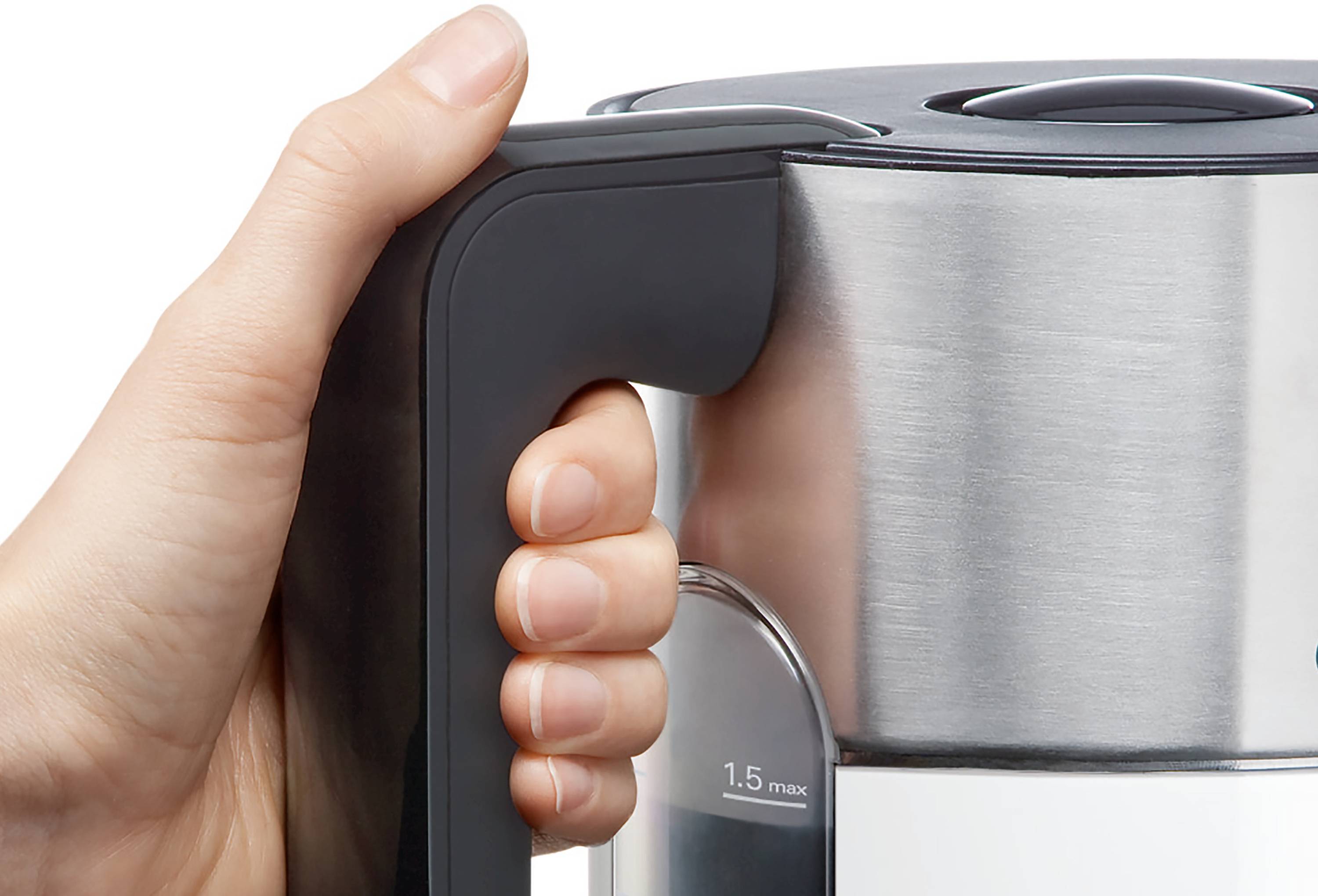 A hand grips the handle of a stainless steel electric kettle, showing a water level indicator marked at '1.5 max'.