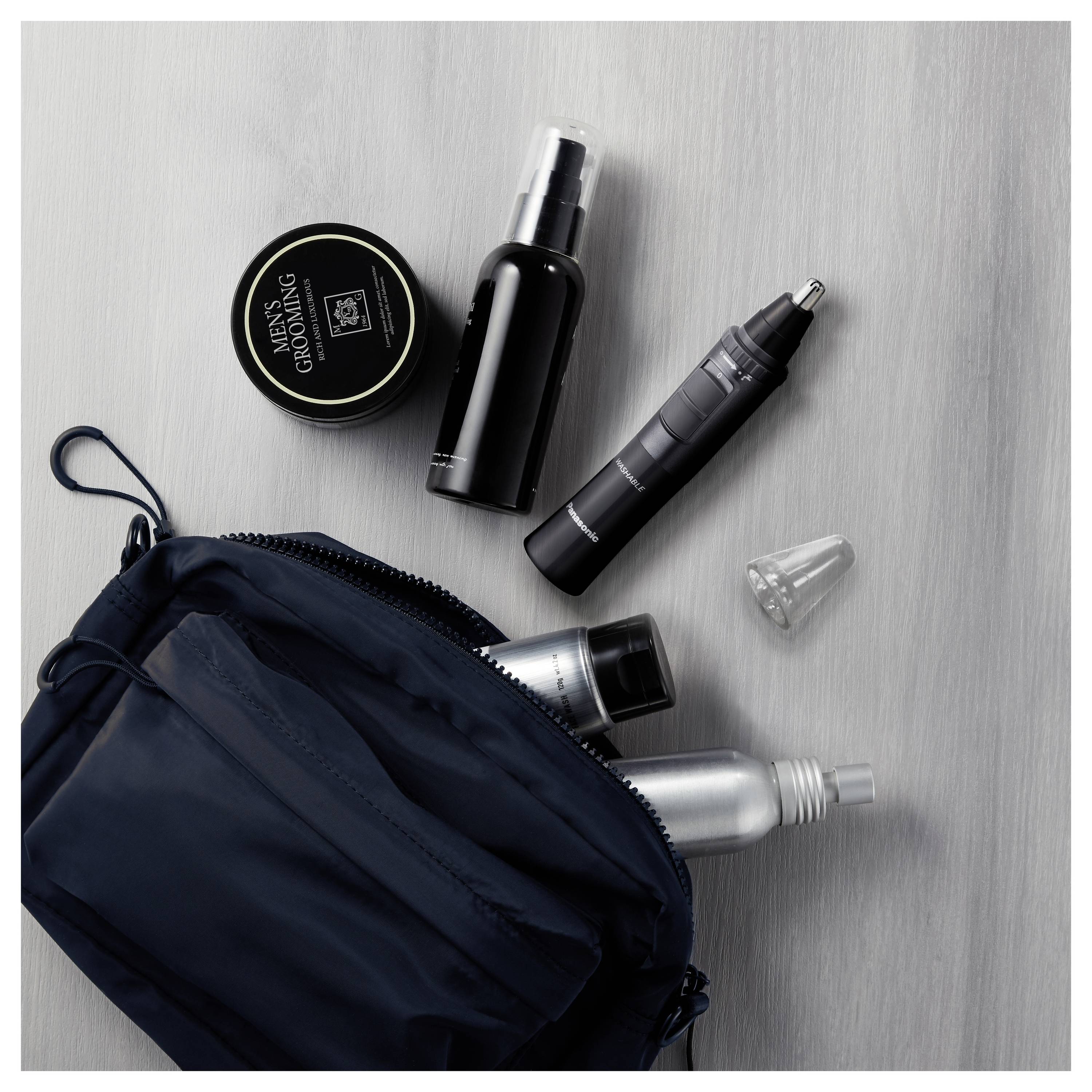A navy toiletry bag partially unzipped, revealing shaving products including a cream tub, spray bottle, nose trimmer, and other grooming items.