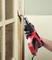 A person uses a red and black heat gun to remove paint from a wooden door frame, highlighting DIY renovation work.