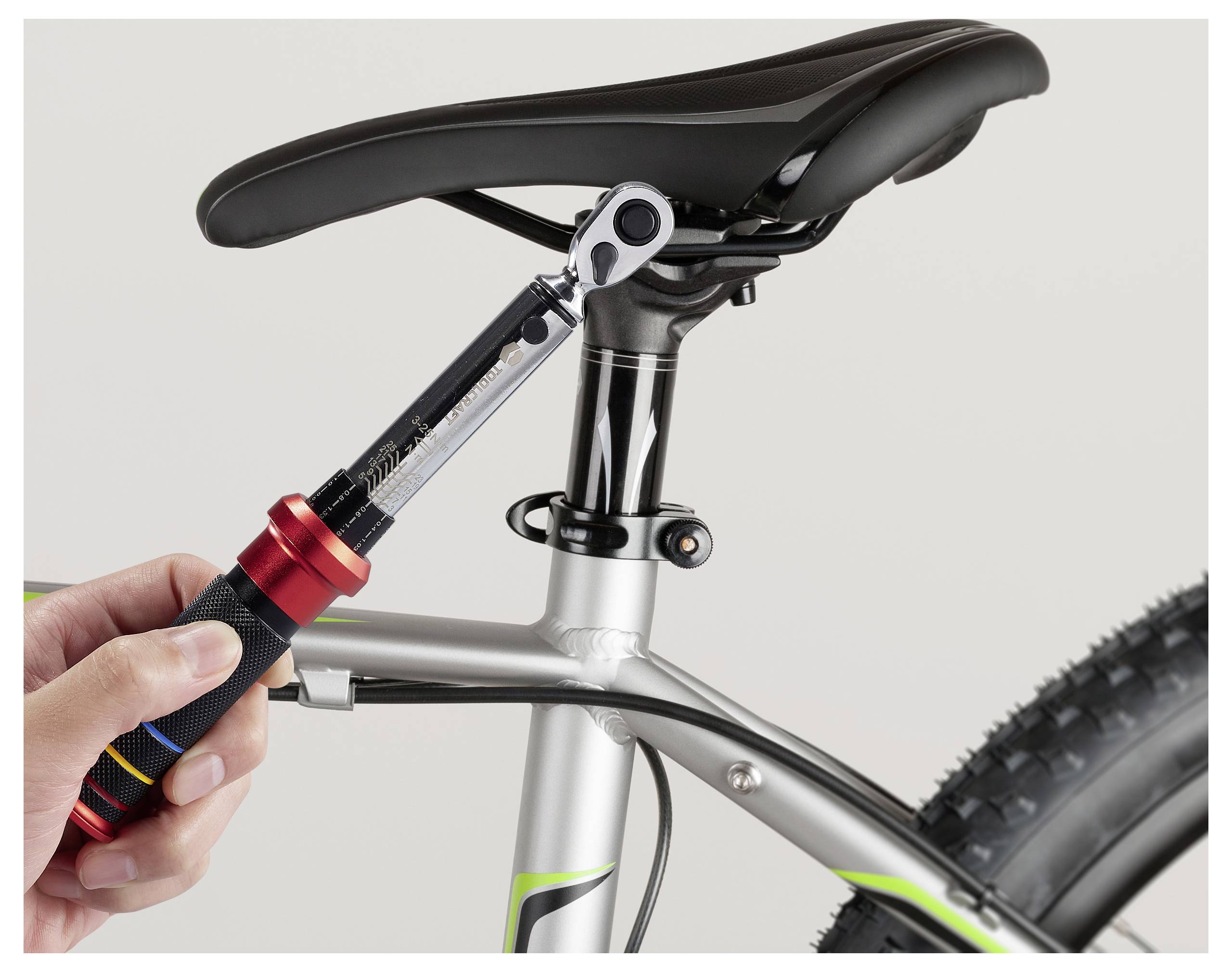A hand tightens the bolt beneath a bike seat with a torque wrench, adjusting the saddle height on a bicycle.