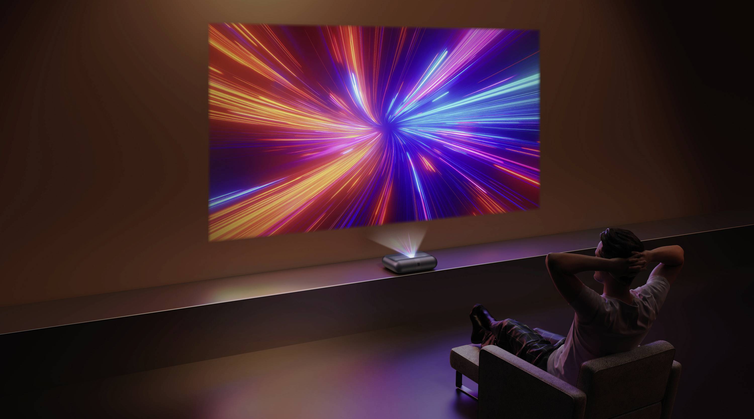 A person sits on a chair, watching a vibrant, colorful light display projected onto a wall in a dimly lit room.