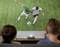 Two people watch a projected image of two soccer players competing for a ball on a grassy field, highlighting a vivid sports scene.