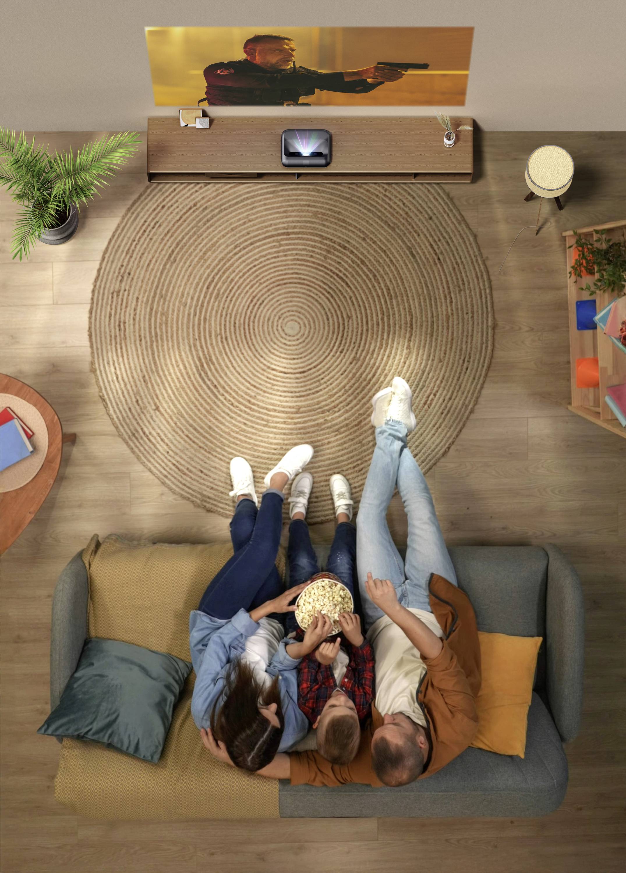 A family of four sits on a sofa, watching an action movie projected on a wall. They're sharing a bowl of popcorn, creating a cozy atmosphere.