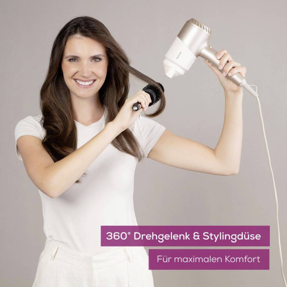 A woman smiles while demonstrating a hairdryer with a 360° swivel joint and styling nozzle.