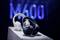 Two pairs of headphones, black and white, are displayed on a pedestal with a blurred 'M600' in blue light in the background.