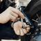 A person uses a wrench to adjust a motorcycle's rear set on a sunny day, focusing on precise mechanical work.