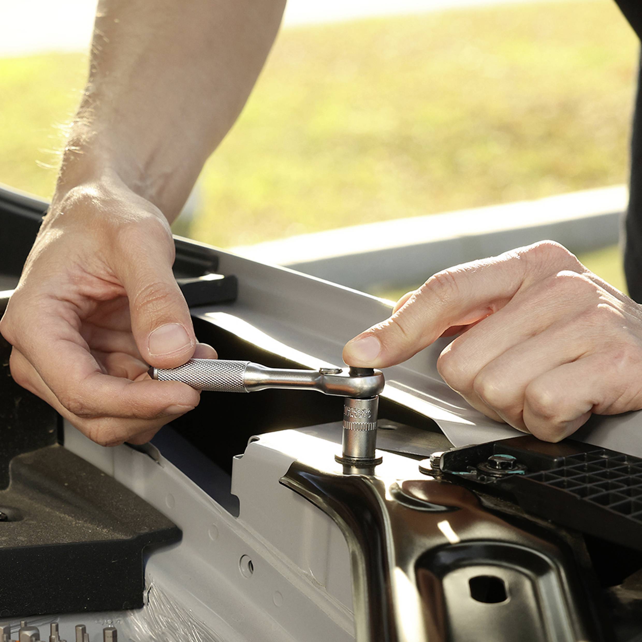 A person uses a ratchet wrench to tighten a bolt on a car engine, showing detailed maintenance work.