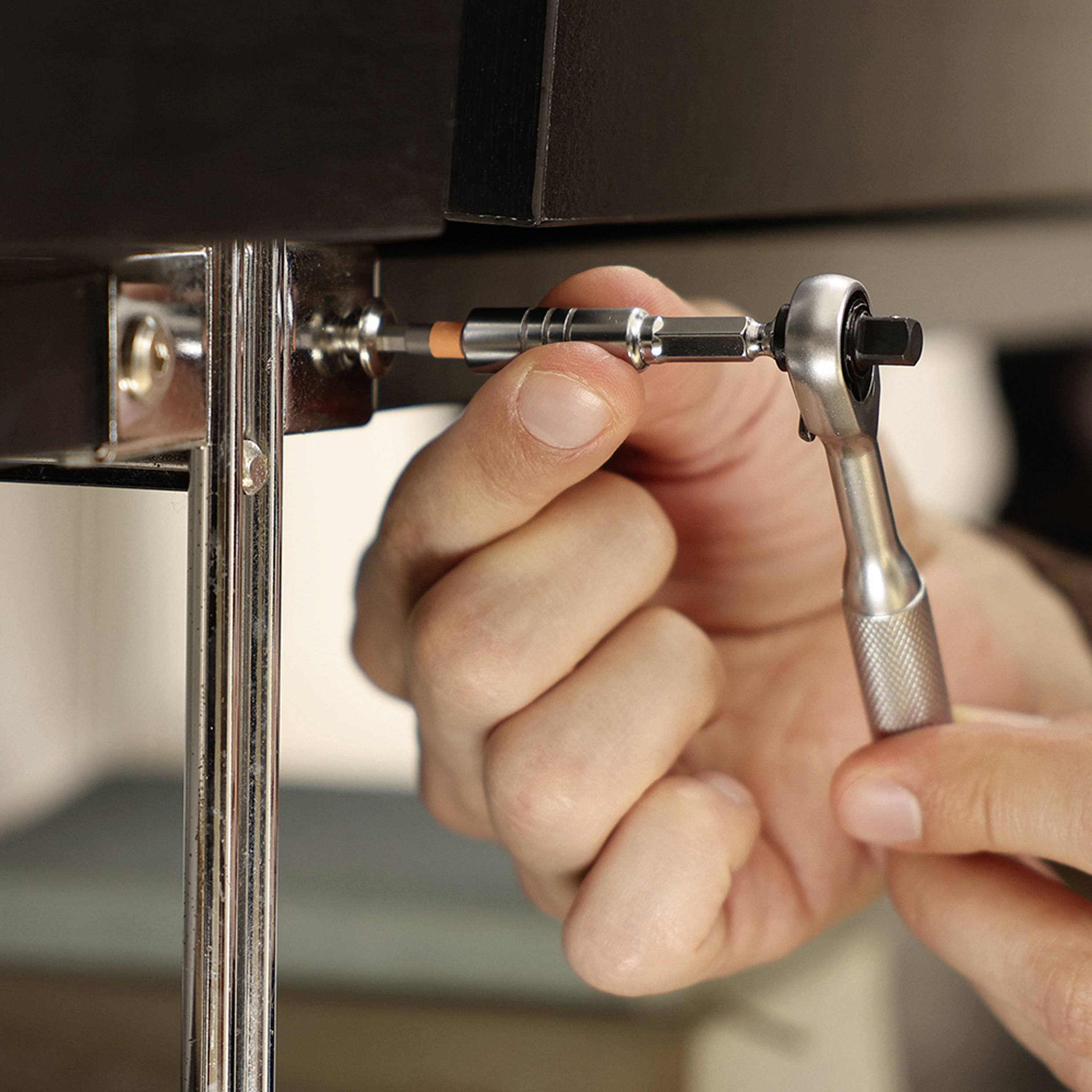 A person is using a ratchet wrench to tighten a bolt on a metallic structure, illustrating a DIY or repair activity.