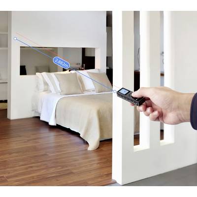 A hand holds a laser measuring device pointed at a bed in a modern room, indicating a distance of 2.882 meters on the display.