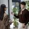 A man and woman conversing indoors. He points to her holding two coffee cups. Text above reads: 'You should buy us a coffee?'