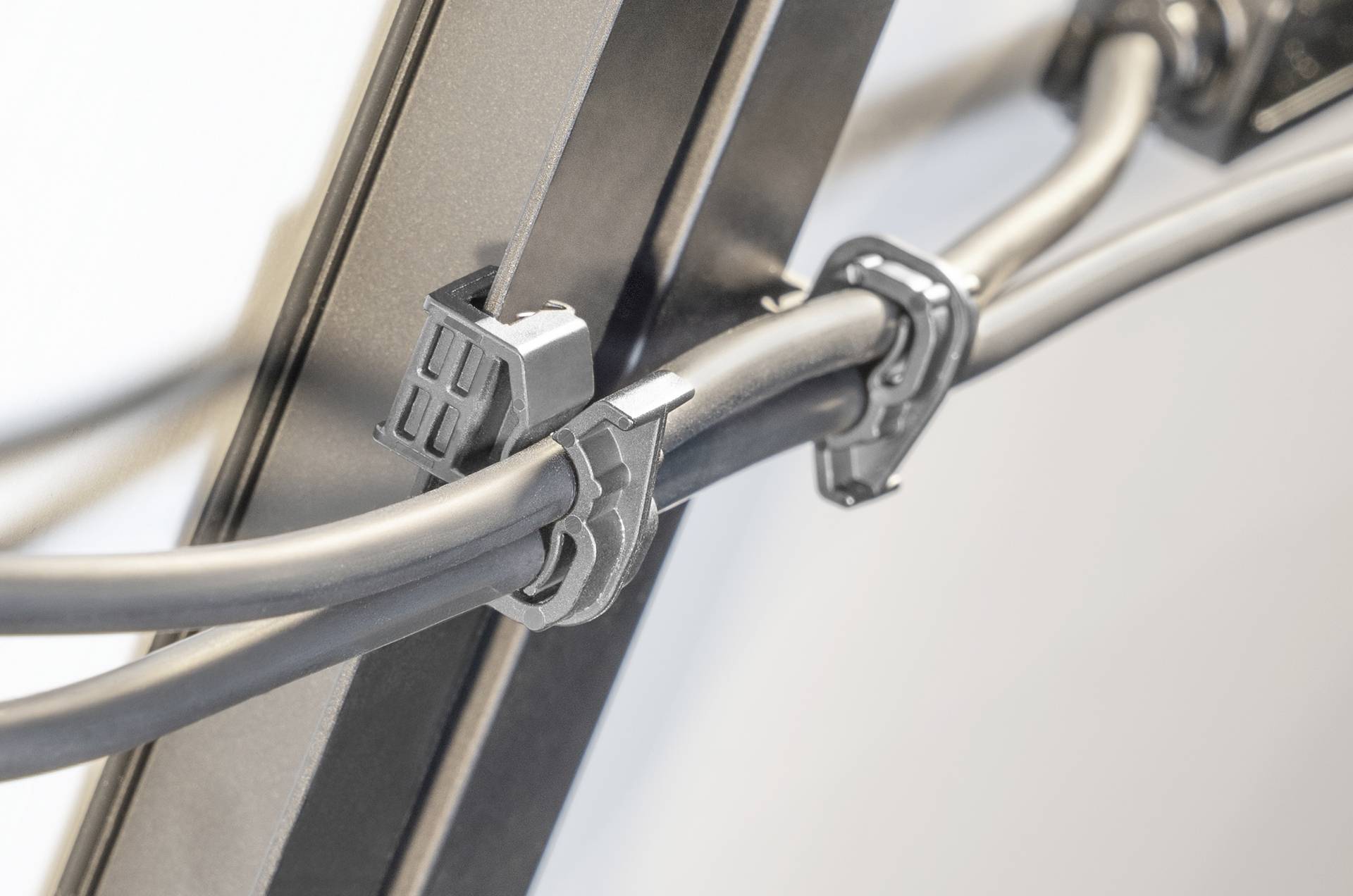 Close-up of two black cables securely fastened with plastic clips to a vertical metal rail on a light-colored wall.