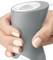 A hand grips a gray ergonomic handle of a device, showing the top view of the handle with a white button on it.