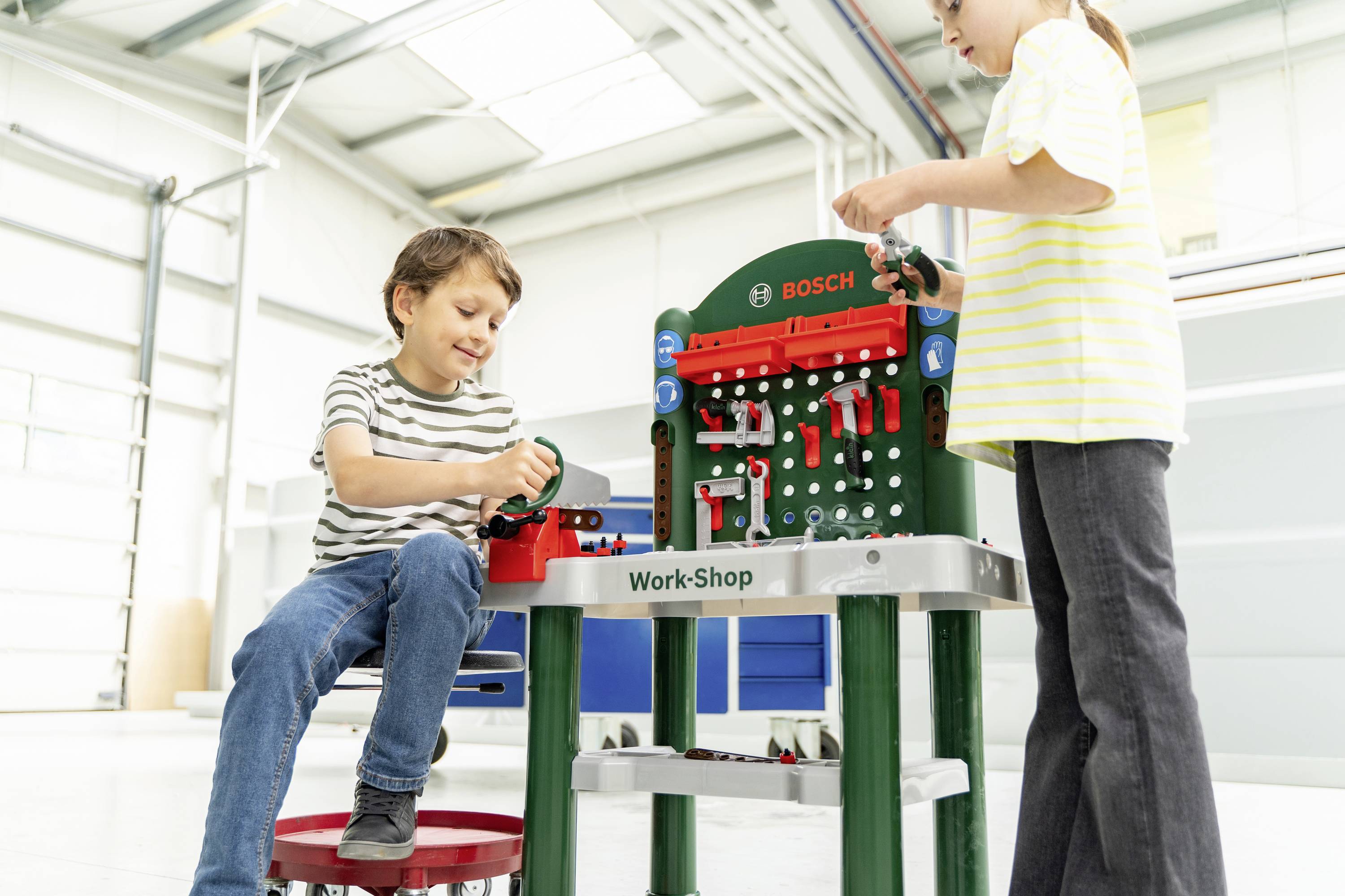 A boy and a girl play with a toy workbench set in a bright room, assembling tools and parts, engaging in imaginative play.