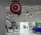 A retractable hose reel with red and black casing is mounted on a garage ceiling. In the background, cars are lifted in a spacious workshop.