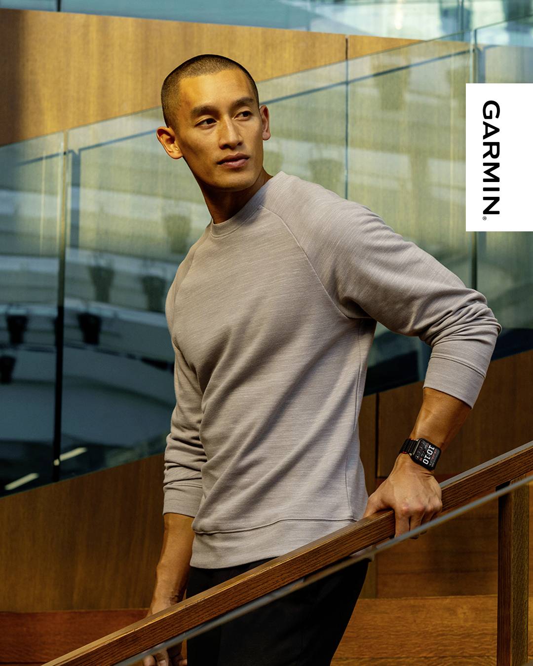 A person wearing a smartwatch stands on a staircase indoors, next to a 'GARMIN' sign. The setting looks modern and sleek.