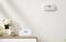 A room with a white teddy bear on a dresser beside a smoke and carbon monoxide detector. Another similar detector is mounted on the wall.