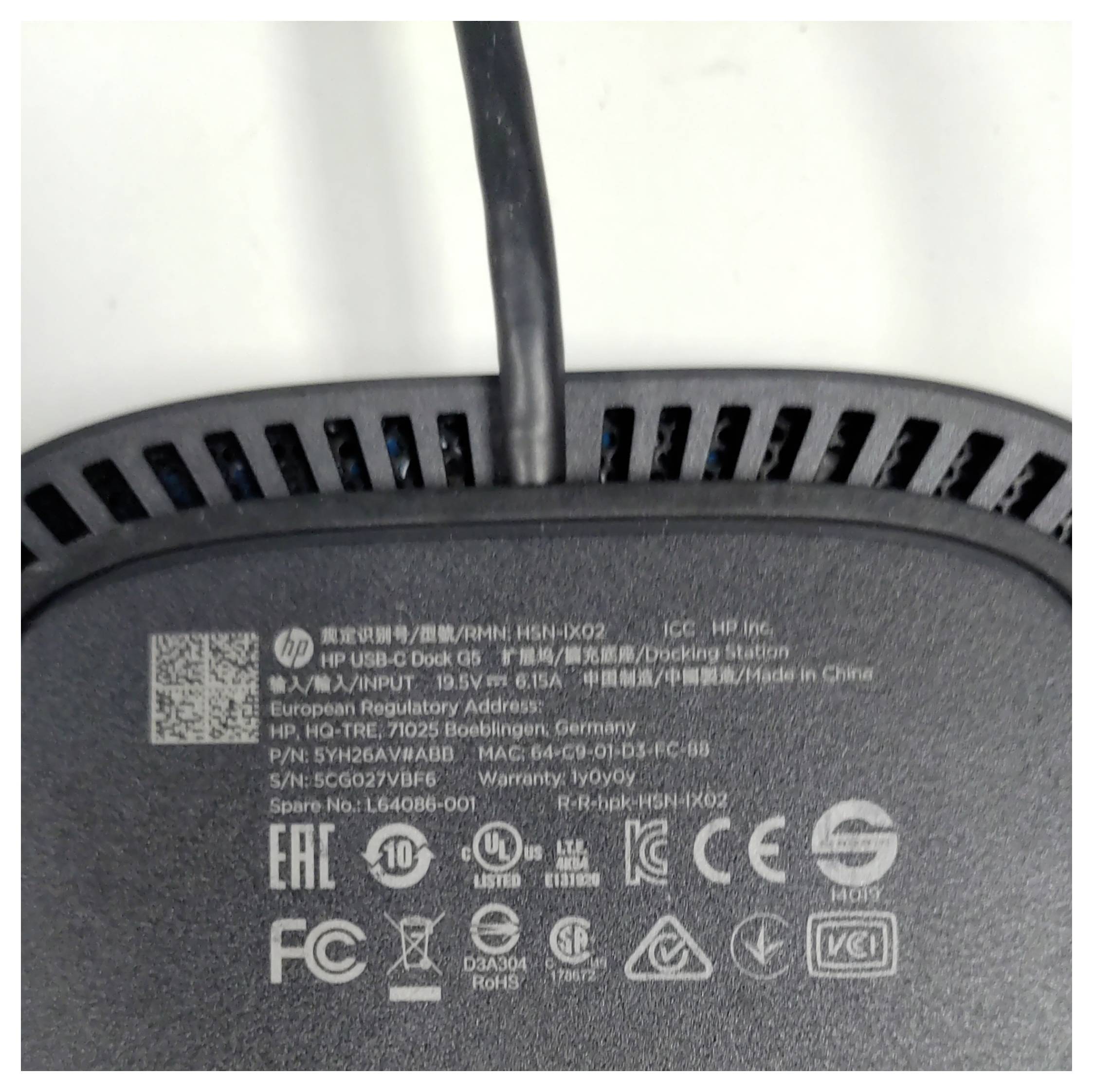 The image shows the bottom of an HP device with various regulatory symbols and certifications printed on it, along with a power cable.