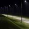 A row of streetlights illuminates a curved, empty road at night, surrounded by grass and darkness, conveying a sense of solitude.