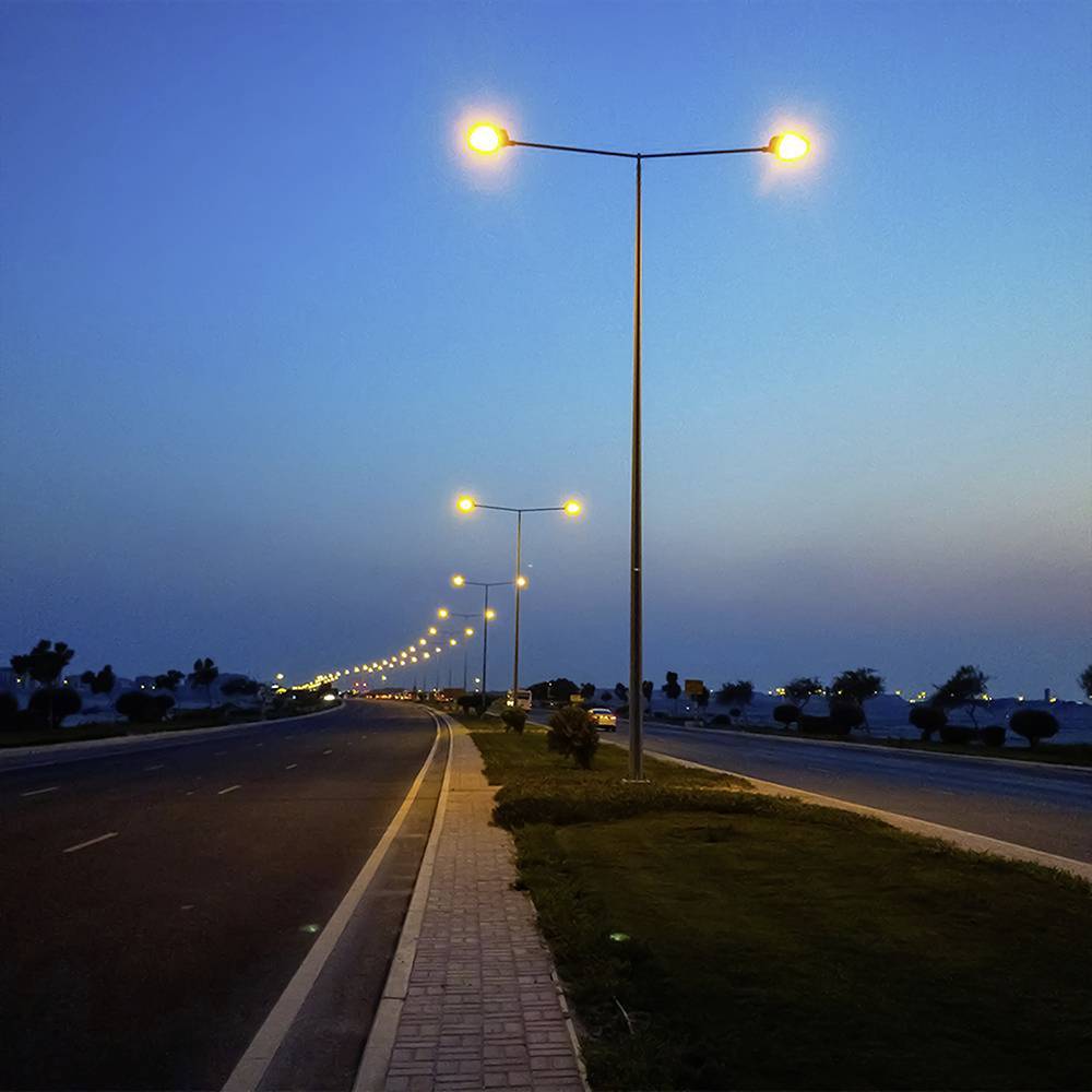 An empty highway at dusk with illuminated streetlights lining both sides, under a clear blue sky.